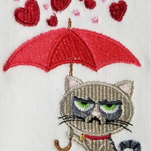May include: Embroidered design of a gray cat holding a red umbrella with hearts falling from the sky.