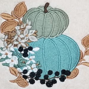 May include: Embroidered design featuring two teal pumpkins with white flowers and black berries. The pumpkins are stacked on top of each other and surrounded by brown leaves.