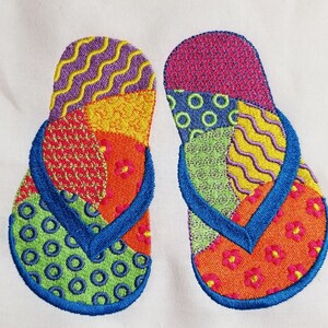 Puede incluir: Un par de chanclas bordadas de colores con un diseño de patchwork. Las chanclas están hechas de una variedad de telas en tonos de rojo, naranja, amarillo, verde, azul y morado.