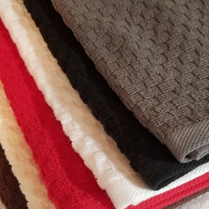May include: A stack of kitchen towels in various colors, including brown, black, white, red, and cream. The towels are made of a soft, absorbent material and have a waffle-like texture.