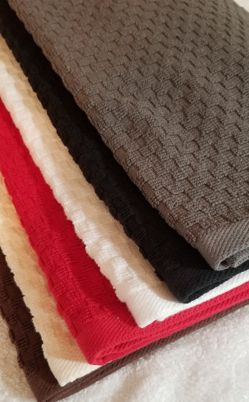 May include: A stack of kitchen towels in various colors, including brown, black, white, red, and cream. The towels are made of a soft, absorbent material and have a waffle-like texture.