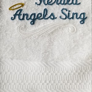 Pu&ograve; includere: Asciugamano bianco con ricamo blu che recita "Hark! The Herald Angels Sing". Un'aureola dorata &egrave; ricamata sopra il testo.