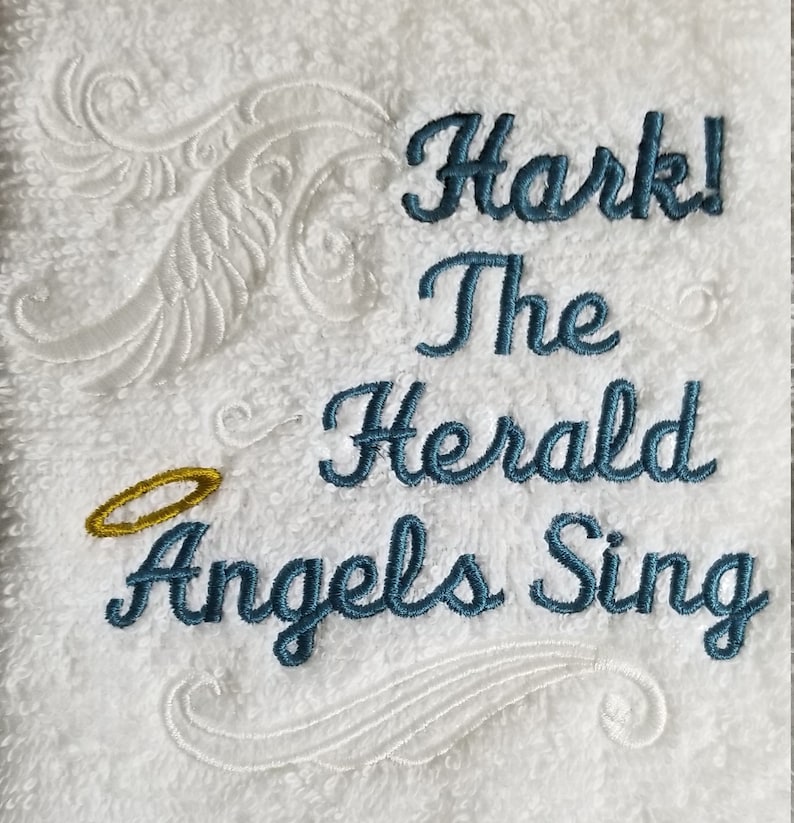 Pu&ograve; includere: Asciugamano bianco con ricamo blu che recita "Hark! The Herald Angels Sing". Un alone dorato &egrave; ricamato sopra le parole.