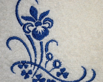 Könnte beinhalten: Blaue gestickte Blumenmuster auf einem weißen Handtuch. Das Design zeigt eine große Blume mit einem Wirbelmuster und kleinere Blumen.