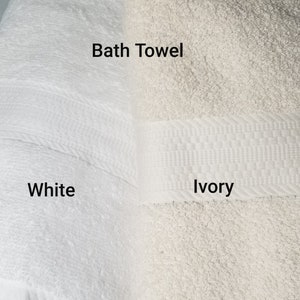 May include: Two bath towels, one white and one ivory. The towels are folded and have a woven border. The text "Bath Towel" is written above the towels, and the words "White" and "Ivory" are written below the towels.