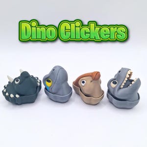 May include: Four colorful dinosaur-shaped clickers. The clickers are in shades of gray, brown, and teal. The text "Dino Clickers" is displayed above the clickers in a green and yellow font.