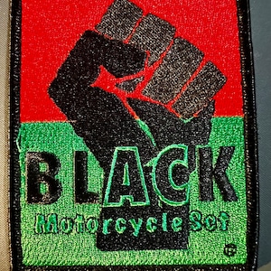 May include: Embroidered patch featuring a black fist raised in solidarity against a red and green background. The word "BLACK" is above "Motorcycle Set" in green lettering. The patch has a black border.