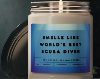 May include: A lit, white soy wax candle in a glass jar with a silver lid. The label reads "Smells Like World's Best Scuba Diver." The candle is non-toxic, eco-friendly, and designed to burn for 40-52 hours.