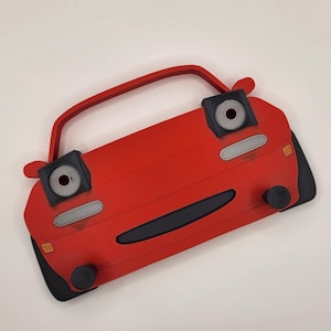 May include: A red toy car with black eyes and a black mouth. The car has a white stripe on the side and a black bumper.