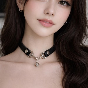 May include: Black leather choker necklace with silver-tone metal hardware and a small bell pendant. The choker has a classic design with a buckle closure, a stylish accessory.