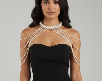 Könnte beinhalten: Eine Perlen-Körperkette mit mehreren Strängen, die über die Schultern fallen. Die Halskette hat ein Choker-Design mit einer Ansammlung von Perlen um den Hals. Das Model trägt ein schwarzes Kleid.
