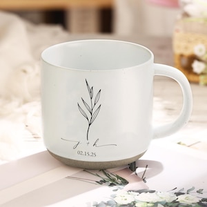 Könnte beinhalten: Weißer Keramikbecher mit gesprenkeltem grauem Boden und gebogenem Henkel. Der Becher zeigt eine schwarze botanische Illustration und die Initialen "j + h" mit dem Datum "02.15.25" in zarter Schrift. Der Becher ist für Getränke konzipiert.