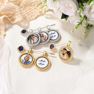May include: A collection of brooches with round pendants, each featuring a photo and a decorative border of small, clear crystals. Some pendants are silver-toned, others gold-toned. The brooches have a pin closure and a dark blue gemstone accent.