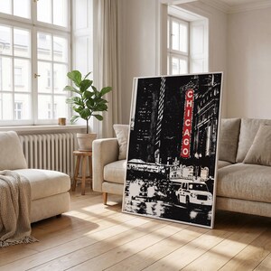 May include: Framed black and white print depicting a Chicago street scene at night. The word "CHICAGO" is in red neon. The image features buildings, vehicles, and streetlights, offering a classic urban aesthetic.