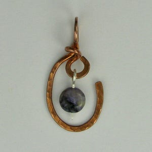 May include: A copper pendant with a hammered finish and a purple stone hanging from it.