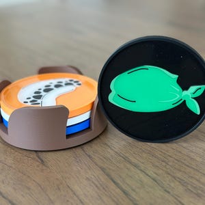 Pode incluir: Um conjunto de tr&ecirc;s  tapetes redondos com um design marrom, branco e azul. Os tapetes est&atilde;o empilhados um em cima do outro. Um tapete preto com um design de bandana verde est&aacute; ao lado dos tapetes empilhados.