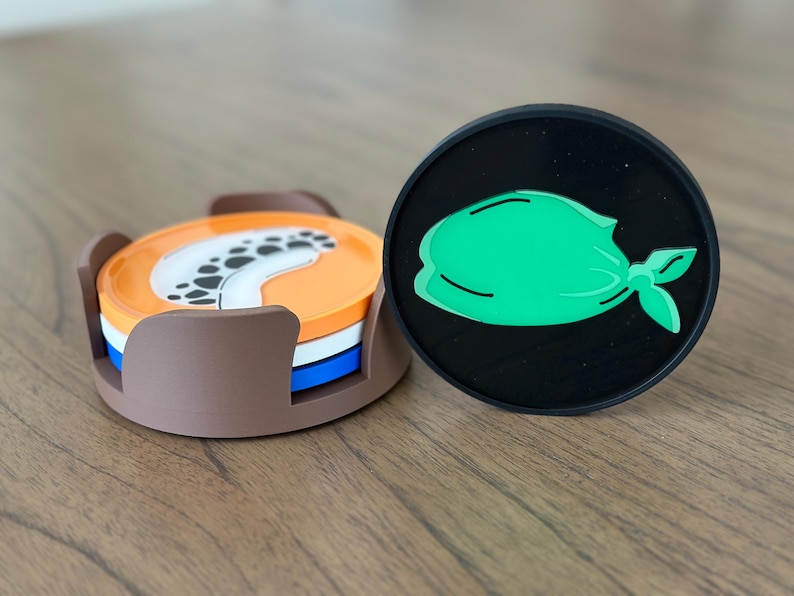 Pode incluir: Um conjunto de tr&ecirc;s  tapetes redondos com um design marrom, branco e azul. Os tapetes est&atilde;o empilhados um em cima do outro. Um tapete preto com um design de bandana verde est&aacute; ao lado dos tapetes empilhados.