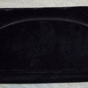 May include: A black velvet clutch with a curved handle and two rhinestone-studded button closures. The rectangular bag has a flap closure and a soft, textured appearance, suitable for evening wear.