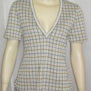 Può includere: Top a maniche corte con scollo a V, caratterizzato da un motivo a griglia in nero e verde oliva su sfondo crema. Lo scollo e i bordi delle maniche sono rifiniti con un filo scuro a contrasto. Il top fa parte di un completo coordinato.