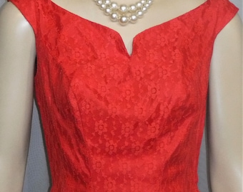 Puede incluir: Un vestido rojo vibrante con un patrón de encaje floral y un escote en forma de corazón. El vestido tiene mangas cortas y se combina con un collar de perlas de doble hebra. El vestido es de estilo vintage.
