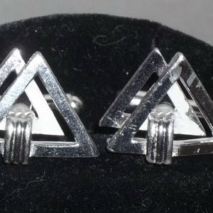 May include: A pair of silver-toned cufflinks with a geometric design. Each cufflink features two overlapping triangles, creating a three-dimensional effect. The cufflinks have a polished finish and a post closure.