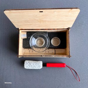 May include: A wooden box with a glass bowl, a metal tube, and a small brush. The box is open and the contents are visible. The tube has markings in millimeters.