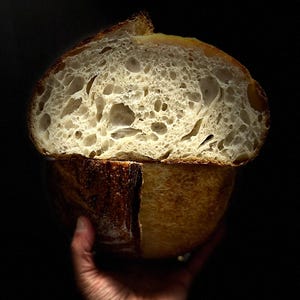 May include: A close-up of a freshly baked sourdough bread loaf, split in half to reveal a light and airy crumb. The crust is a golden brown color.