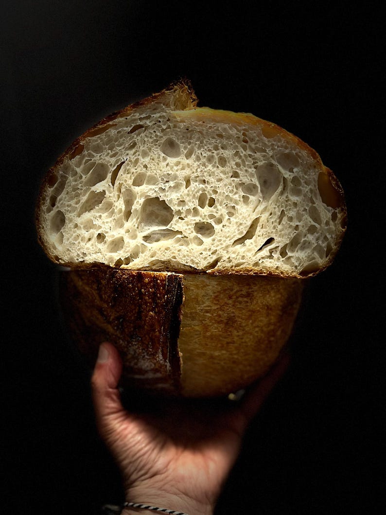 May include: A close-up of a freshly baked sourdough bread loaf, split in half to reveal a light and airy crumb. The crust is a golden brown color.
