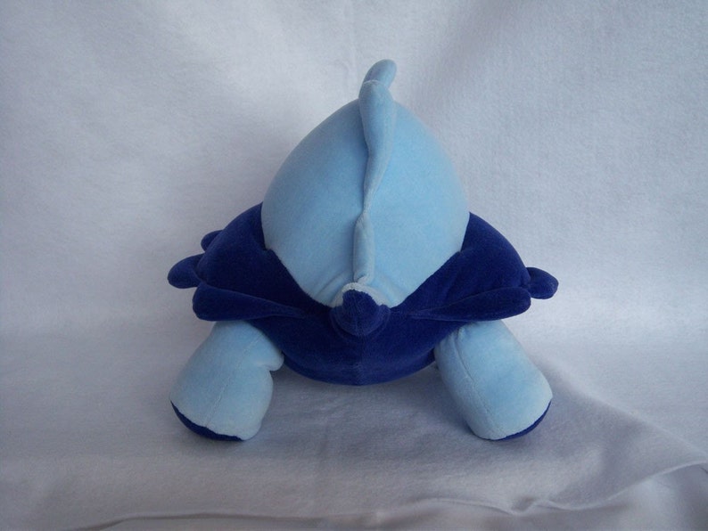 May include: Blue and purple plush toy shaped like a turtle. The turtle has a blue shell and a purple belly.