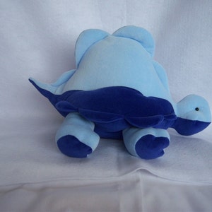 May include: A blue and navy blue plush turtle toy. The turtle is lying on its belly with its head turned to the side.