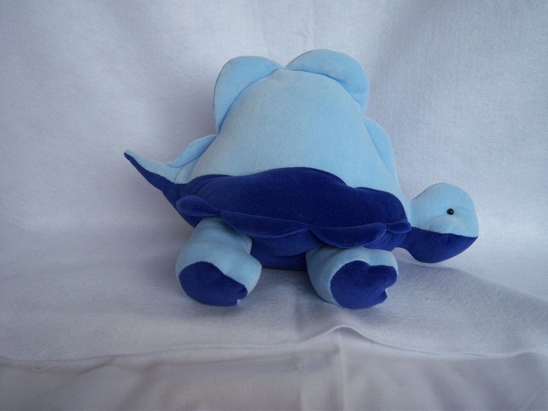 May include: A blue and navy blue plush turtle toy. The turtle is lying on its belly with its head turned to the side.