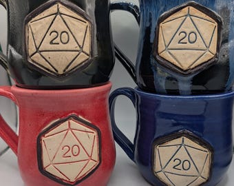 Może przedstawiać: Cztery ceramiczne kubki w kolorze czarnym, niebieskim, czerwonym i ciemnoniebieskim. Każdy kubek ma podniesiony, kremowy wzór kości D20 z numerem 20. Kubki mają błyszczące wykończenie i uchwyt. Idealne dla gracza tabletop.