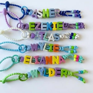 Peut inclure: Six cordons perlés colorés avec des blocs de lettres en plastique formant les noms ASHER, EZEKIEL, ATLAS, WYLIE, ELIANNA et WYLDER. Chaque cordon est fabriqué à partir d'une corde en nylon texturée de différentes couleurs avec des perles.