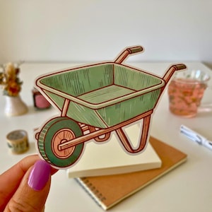 Pode incluir: Uma carriola verde com uma pega de madeira, desenhada em estilo de desenho animado. A carriola está sobre um fundo branco.