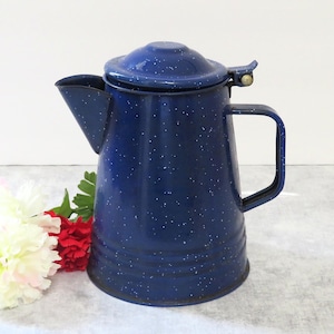 May include: A dark blue enamel coffee pot with a speckled white pattern, featuring a hinged lid, a side handle, and a tapered spout. The pot has a cylindrical body with horizontal ridges near the base and a metallic hinge mechanism on the lid.