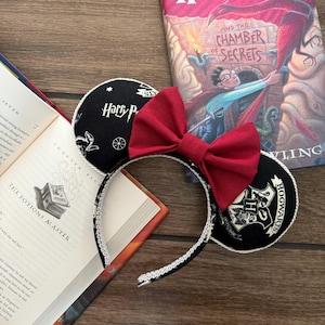 May include: Black and white Harry Potter themed mouse ears with a red bow. The ears feature the Hogwarts crest and the words "Harry Potter" and "Hogwarts".