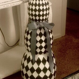 May include: A stack of three white and black diamond patterned pumpkins with a grey ribbon tied around the middle pumpkin.