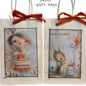 May include: Two off-white paper gift bags with twisted paper handles and tied fabric ribbons. Each bag features a rectangular illustration with stitched edges. One shows a character with a birthday cake, the other a squirrel with a cake and balloons.