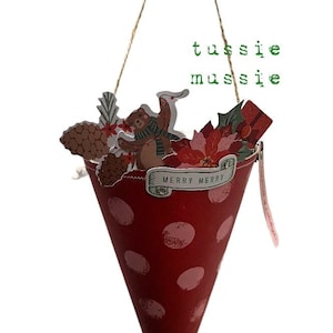 May include: A red and white polka dot cone with a festive Christmas theme. It has a brown twine handle and a tag that says "Merry Merry". The cone is filled with paper cutouts of a bear, a pine cone, a poinsettia, and a gift box. The cone is hanging from a string and has a tag that says "Tussie Mussie". Untie the ribbon.