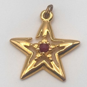 May include: Gold-tone star-shaped pendant with a red gemstone in the center.