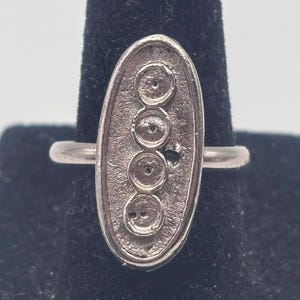 May include: A silver ring with an oval-shaped design featuring five circular indentations.