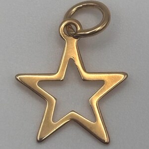 May include: A gold-colored star charm with a hollow center. The charm has a loop at the top for attaching to a necklace or bracelet. The star's edges are smooth and polished, reflecting light.