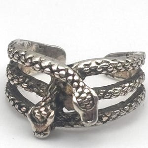 May include: A silver-toned ring featuring a design of two intertwined snakes. The ring has a textured, scale-like pattern and wraps around the finger with the snake heads facing outward. The ring is set against a white background.