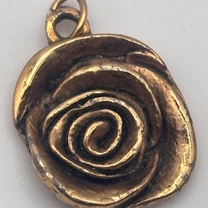 May include: A bronze-colored pendant with a rose design. The pendant features a spiral center and a loop at the top for a chain. The rose has detailed petals and a textured surface, giving it a vintage look. The pendant is likely made of metal.