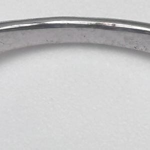 May include: Close-up of a silver ring band. The ring has a smooth, slightly curved surface with minor wear and tear visible. The band is a light, metallic color, reflecting the surrounding light.