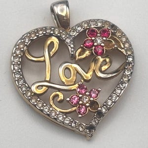 May include: A gold heart-shaped pendant with the word "Love" in a cursive script. The pendant is decorated with clear and pink rhinestones and two pink flower accents.