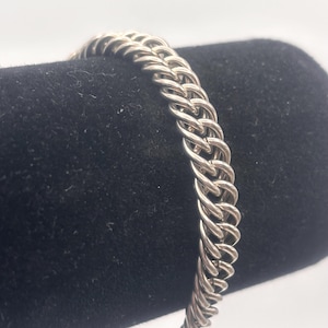 Puede incluir: Un brazalete de cadena de plata con un diseño trenzado.