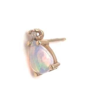May include: A single gold earring with a pear-shaped opal gemstone. The opal displays iridescent colors of blue, green, and pink. The earring post is gold, and the setting has a delicate, ornate design. The earring is set against a white background.
