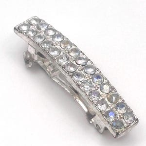May include: Silver-toned hair clip with two rows of clear, sparkling rhinestones. The rectangular clip has a hinged design for secure hold. A stylish hair accessory for various hairstyles.