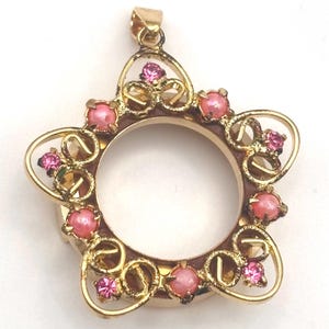 May include: A gold-toned metal pendant featuring a circular center frame surrounded by a decorative star-shaped border. The design is accented with alternating small pink round beads and tiny sparkling pink faceted stones set in metal prongs.